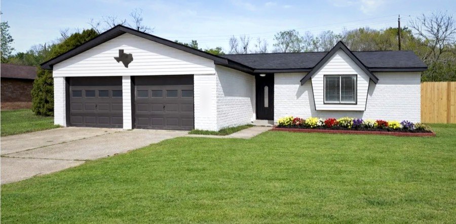 The front of The Serenity Passage home: white brick, black roof and a flower bed along the walkway